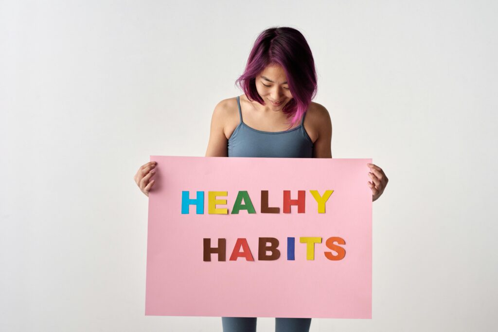 Asian woman holding a colorful 'Healthy Habits' sign in a studio setting, promoting wellness.