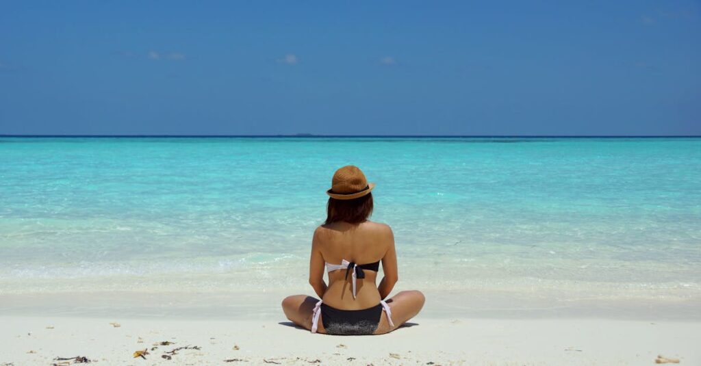 Rear view of a woman in a bikini and hat relaxing on a pristine beach in Maldives.